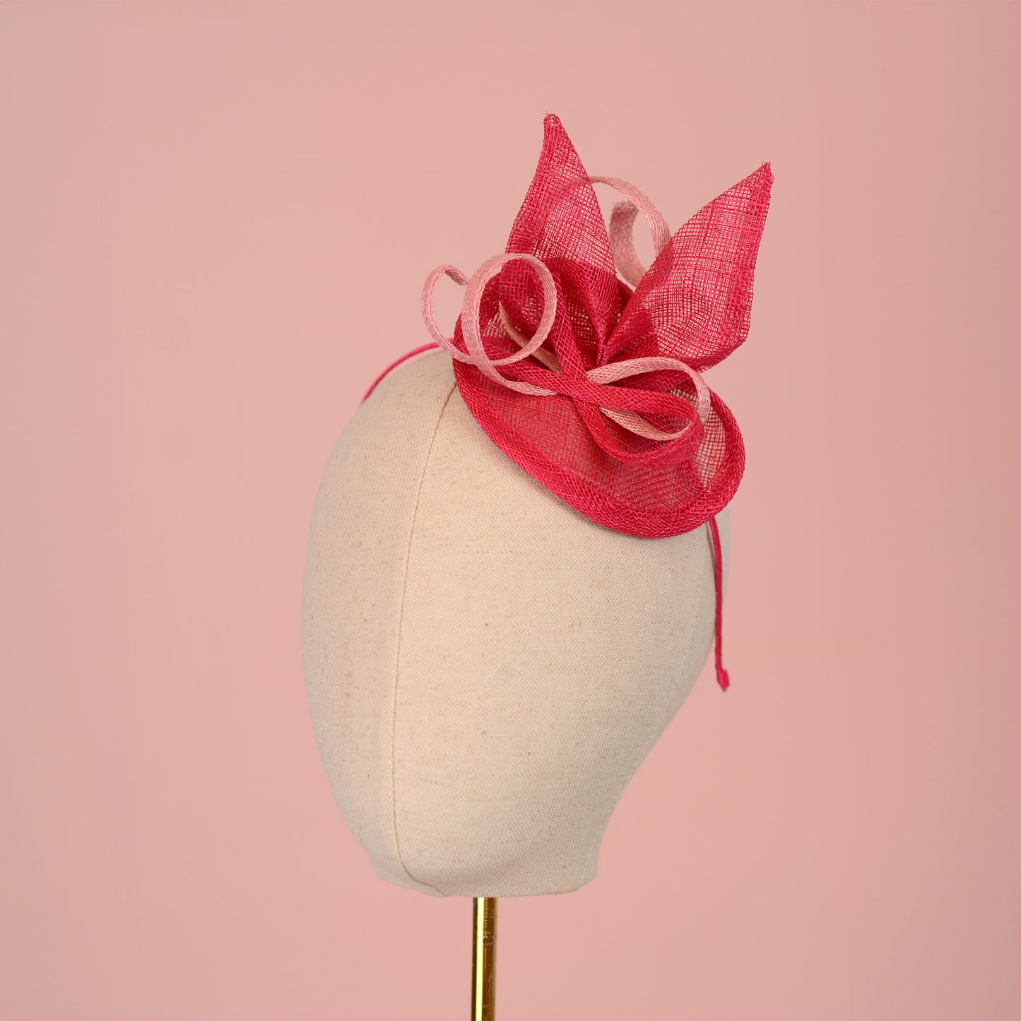 A pink sinamay side perching fascinator in two shades of tonal pink displayed on a mannequin head against a pink background