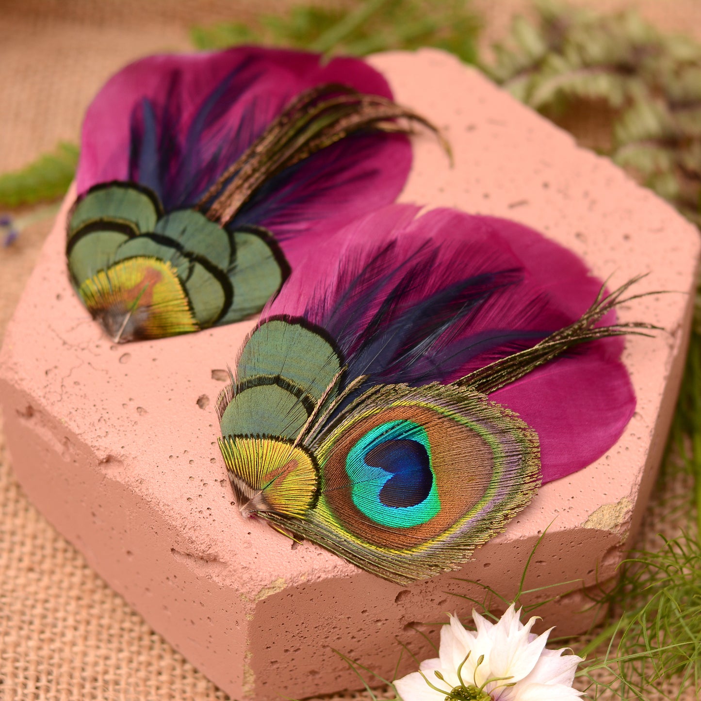 close up of matching purple peacock feather hair clips on a pink stone