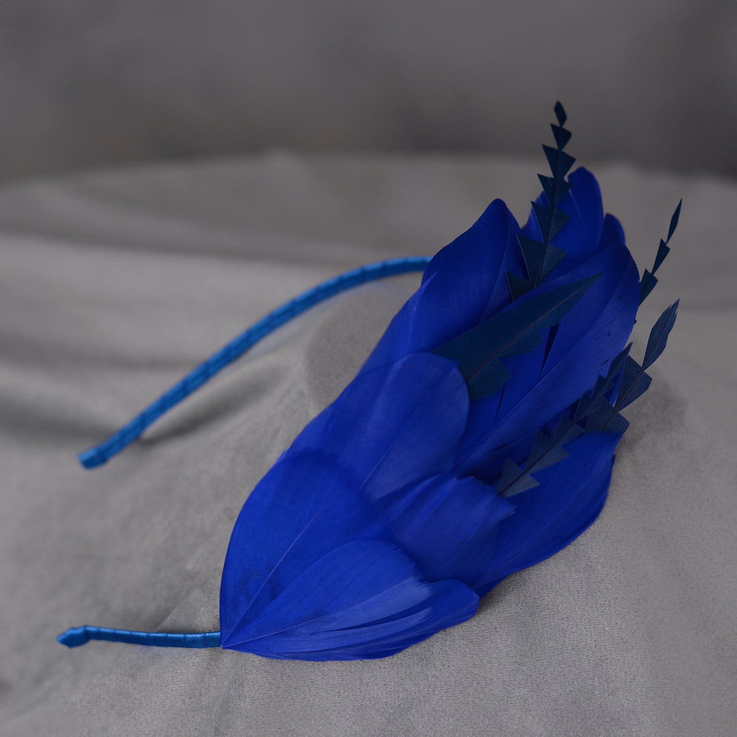 Blue feathered headband on a mannequin head against a grey background
