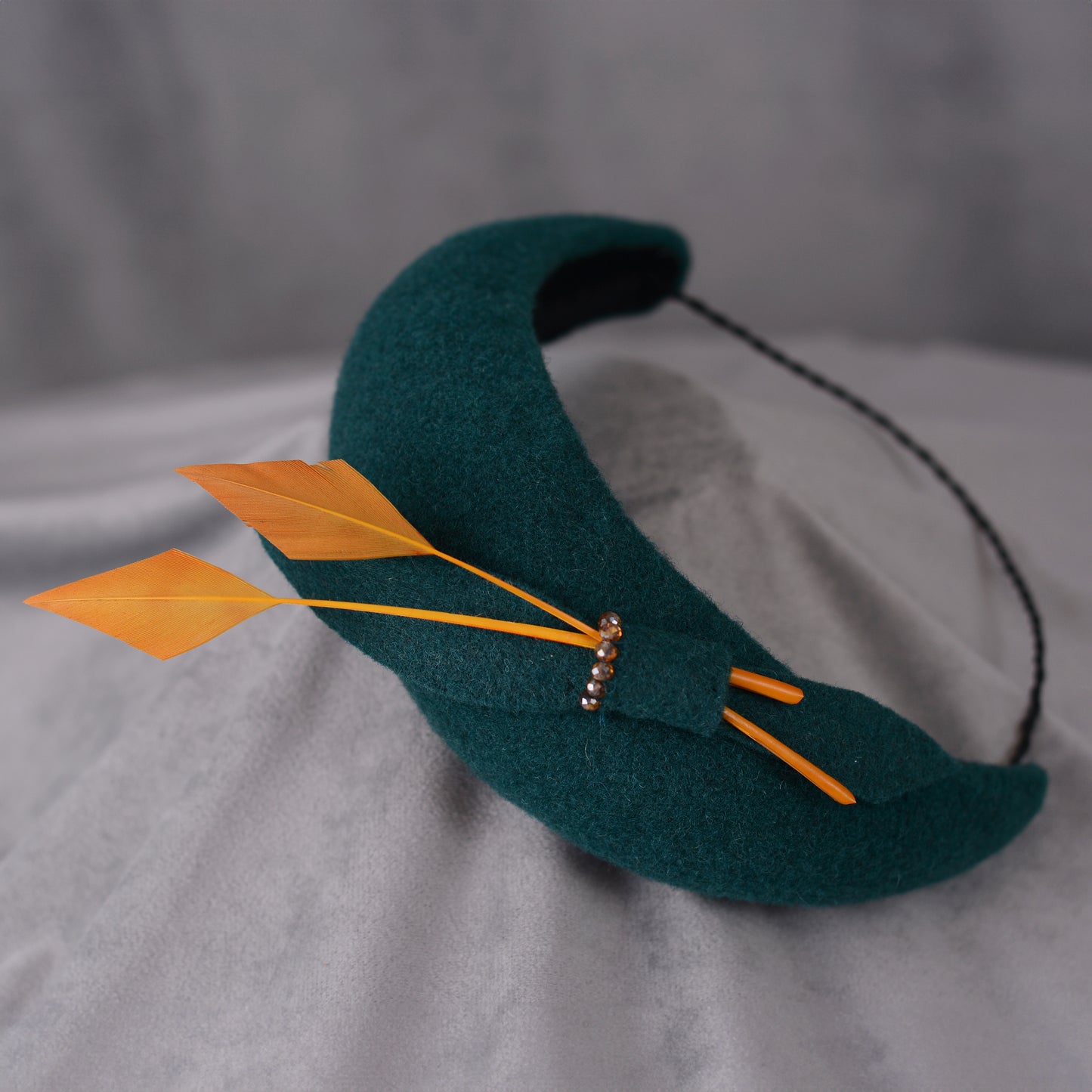 Teal green headband fascinator with gold yellow feathers and bow on a gray background
