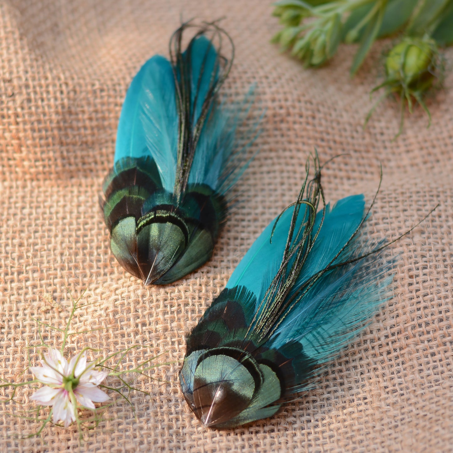 teal feather hair clip with iridescent green feathers on a burlap background with flowers