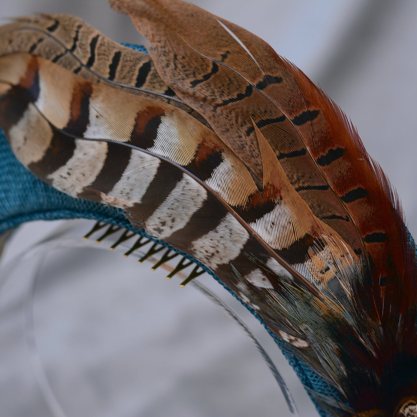 Close up of a teal blue occasion headband with feather accents on a grey background