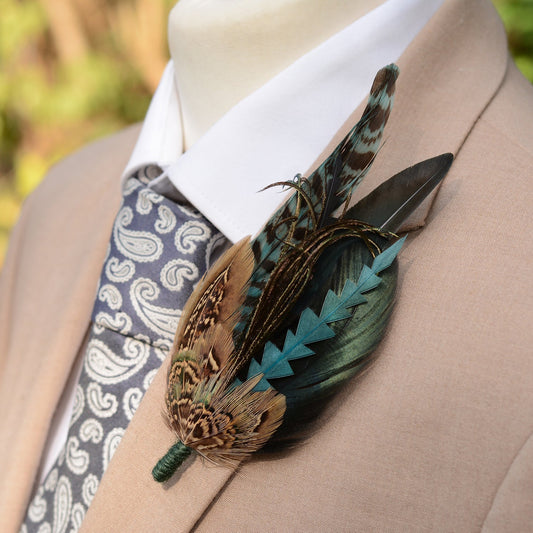 A large teal and green statement feather boutonniere on a mannequin with a paisley tie and beige suit jacket.