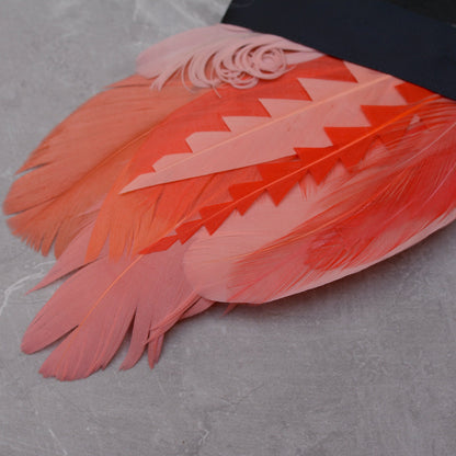 Close up of a tropical-style feather pocket square in shades of coral and pink laid on a grey stone.