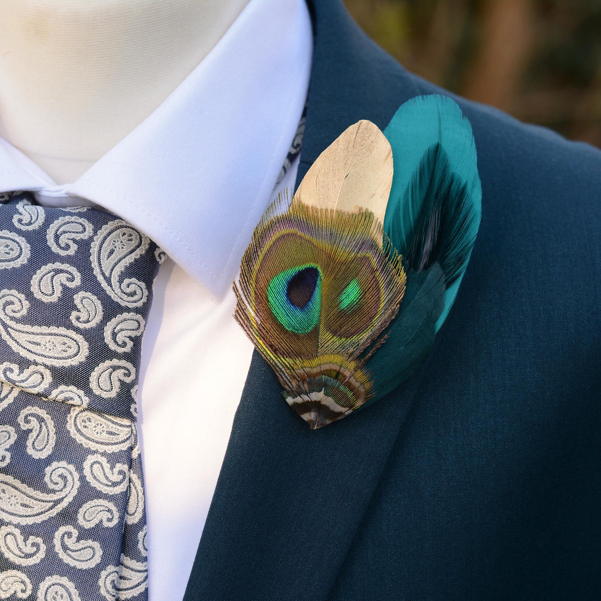 Teal and gold peacock feather brooch pin boutonniere on a teal suit with white shirt and pale blue paisley tie.
