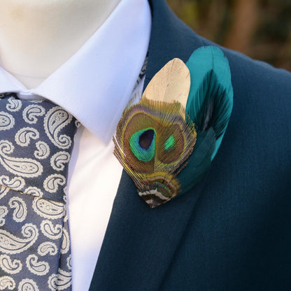 Teal and gold peacock feather brooch pin boutonniere on a teal suit with white shirt and pale blue paisley tie.