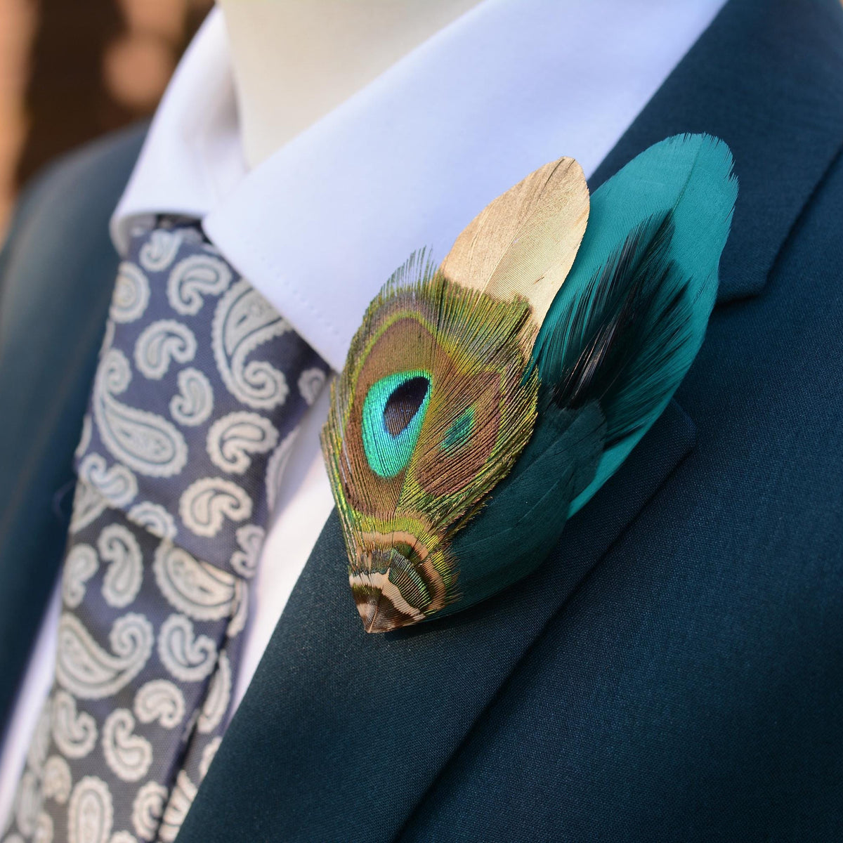 Teal and gold peacock feather brooch pin boutonniere on a teal suit with white shirt and pale blue paisley tie.