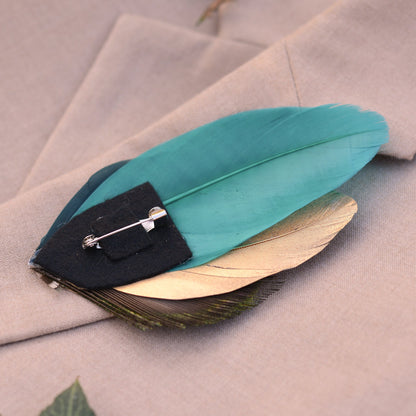 Teal feather brooch on a beige fabric background