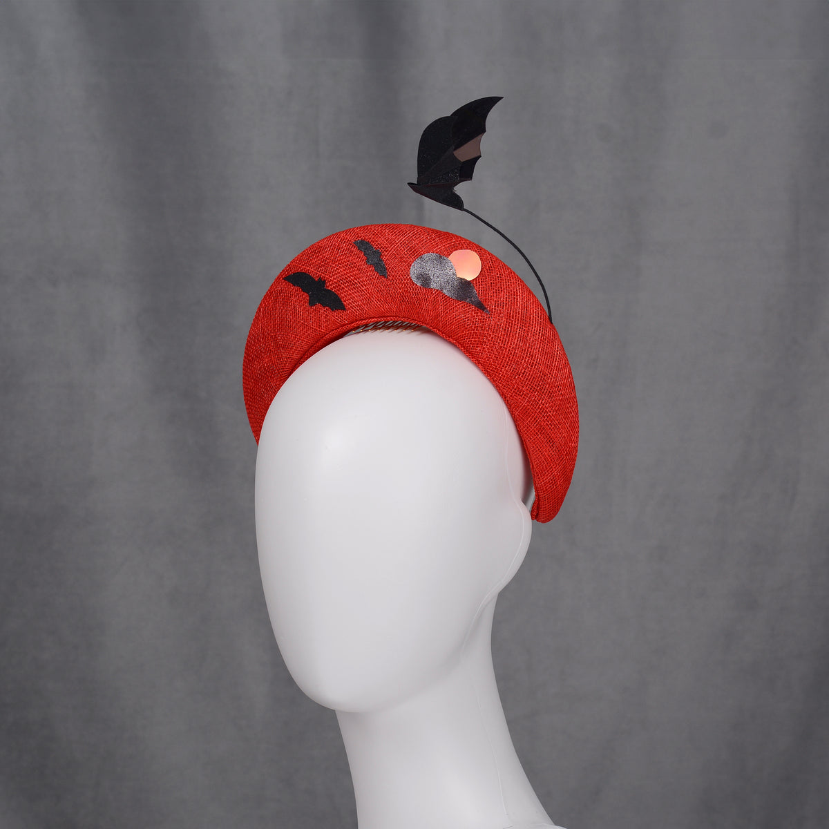A red halo headband decorated with bat and cloud motifs. The headband has a curved form and is embellished with black bat silhouettes on the back and a bat-shaped decoration rises from the headband.