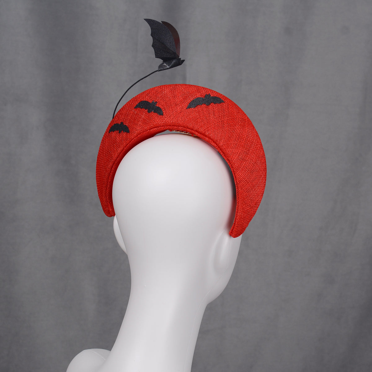 A red halo headband decorated with bat and cloud motifs. The headband has a curved form and is embellished with black bat silhouettes on the back and a bat-shaped decoration rises from the headband.