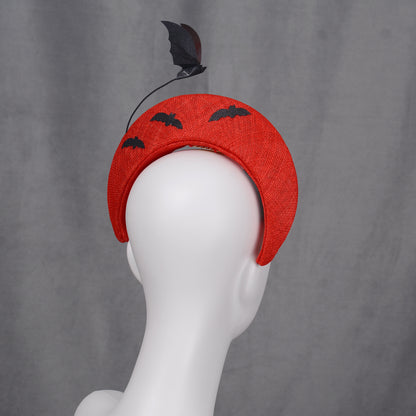 A red halo headband decorated with bat and cloud motifs. The headband has a curved form and is embellished with black bat silhouettes on the back and a bat-shaped decoration rises from the headband.