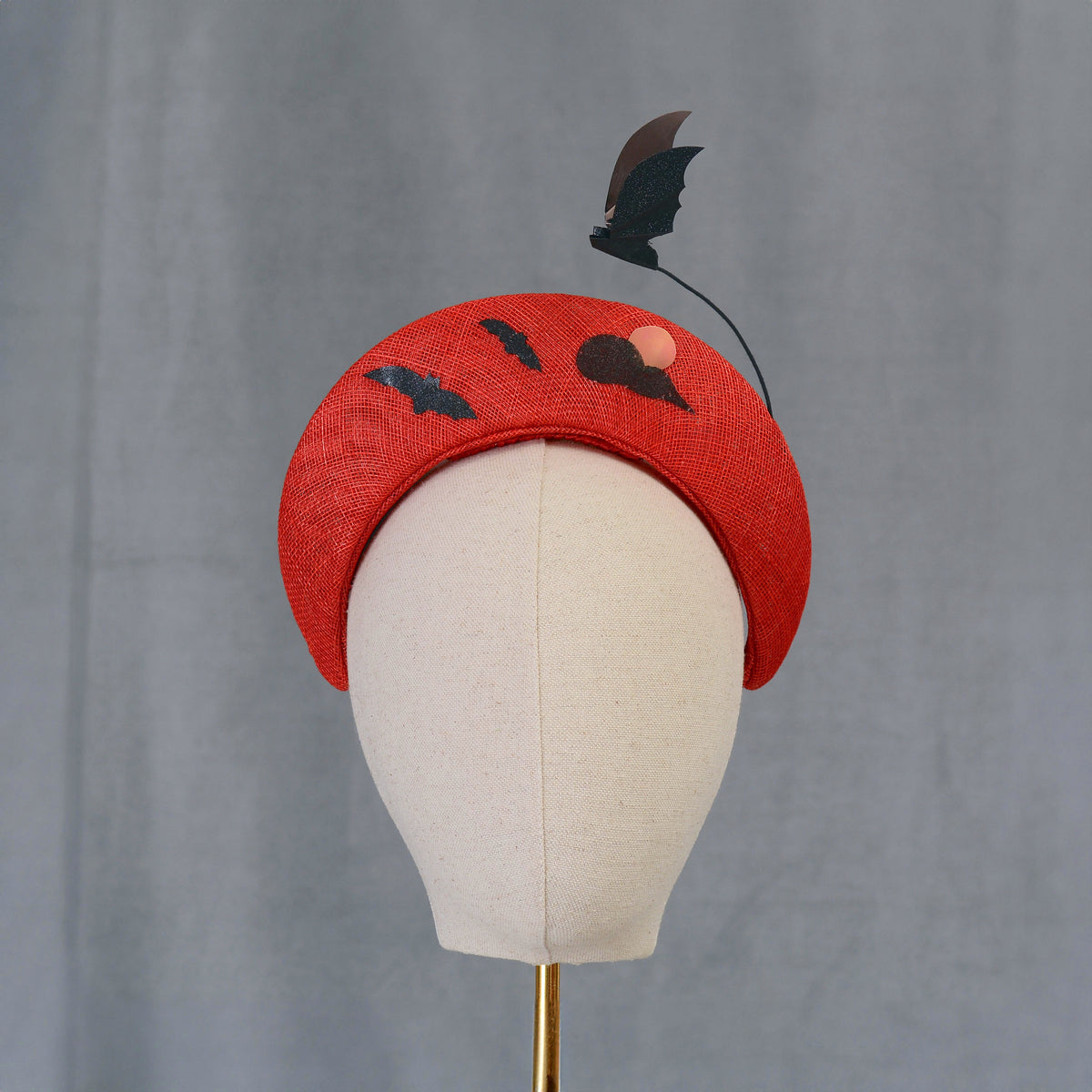 A red halo headband decorated with bat and cloud motifs. The headband has a curved form and is embellished with black bat silhouettes and a cloud with a  metallic pink circle forming a  blood moon. A bat-shaped decoration rises from the headband.