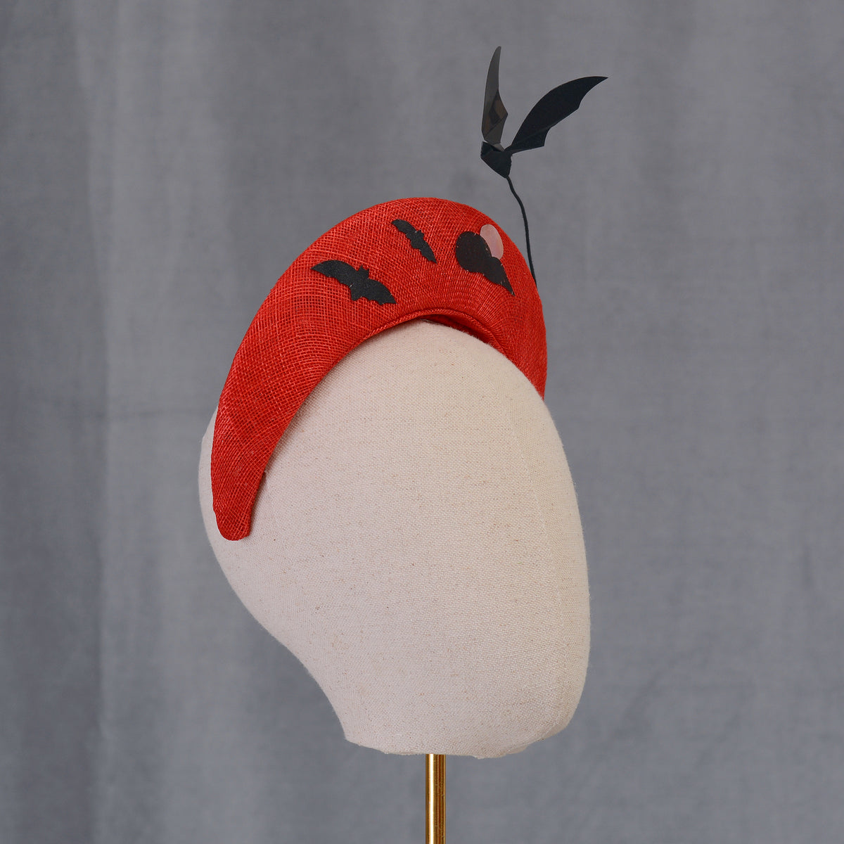  A red headband with black bat and cloud designs. The headband is made of a woven straw material and features a floating decorative bat accent. Suitable for Halloween or themed events.