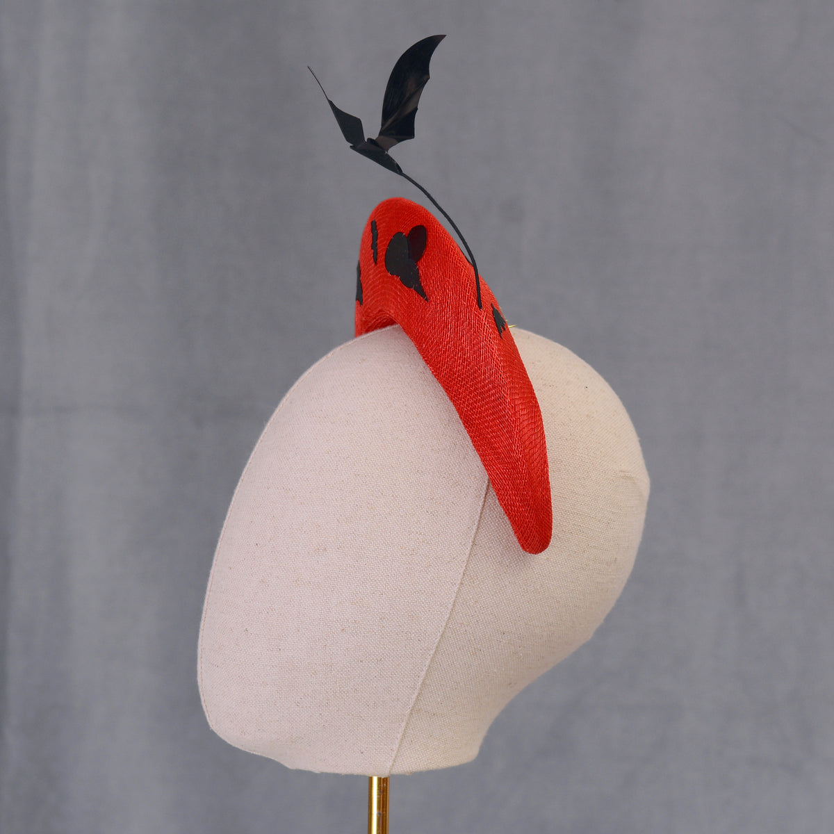 A vibrant red headpiece with black detailing, including a bat-shaped feature. The headpiece is displayed on a mannequin head, highlighting its shape and design. Perfect for special halloeen themed events and parties.