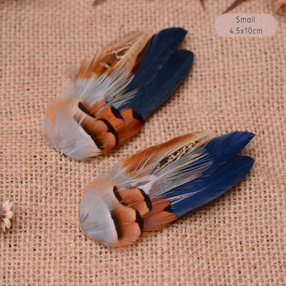 Two small decorative feather hair pieces with blue, brown, white, and black feathers, placed on a beige burlap background.