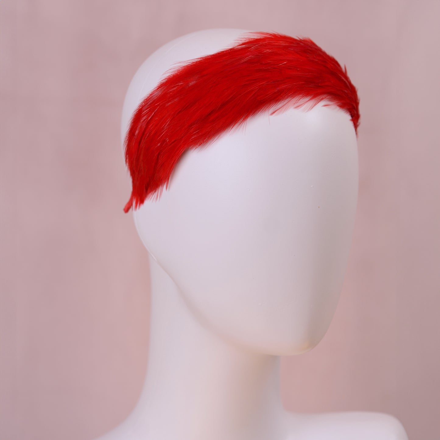 A bright red feather wedding headpiece displayed on a white mannequin head against a soft pink background.