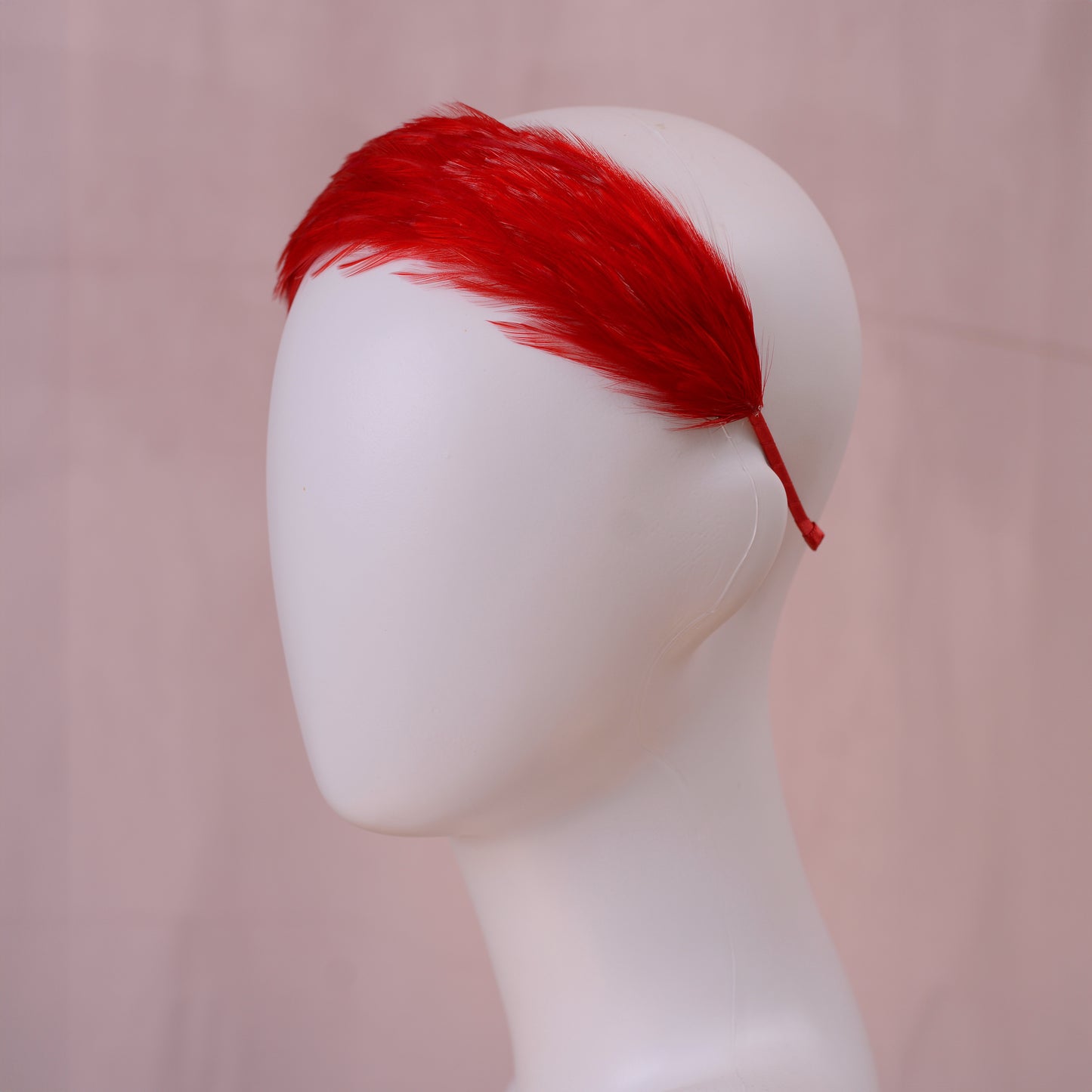 A bright red feather wedding headband displayed on a white mannequin head against a soft pink background.