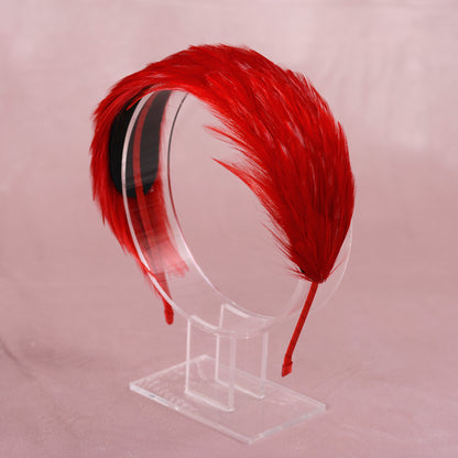 A vibrant red feather headband displayed on a clear acrylic stand against a soft pink background.