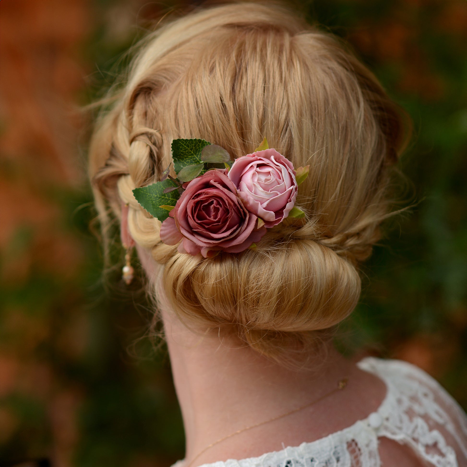 Blonde hair styled in an updo with fabic flower hair clip of soft pink roses, blurred natural background