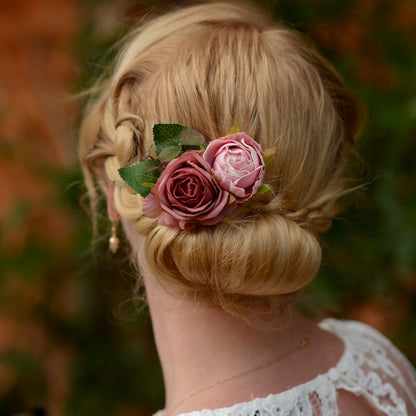 Blonde hair styled in an updo with fabic flower hair clip of soft pink roses, blurred natural background