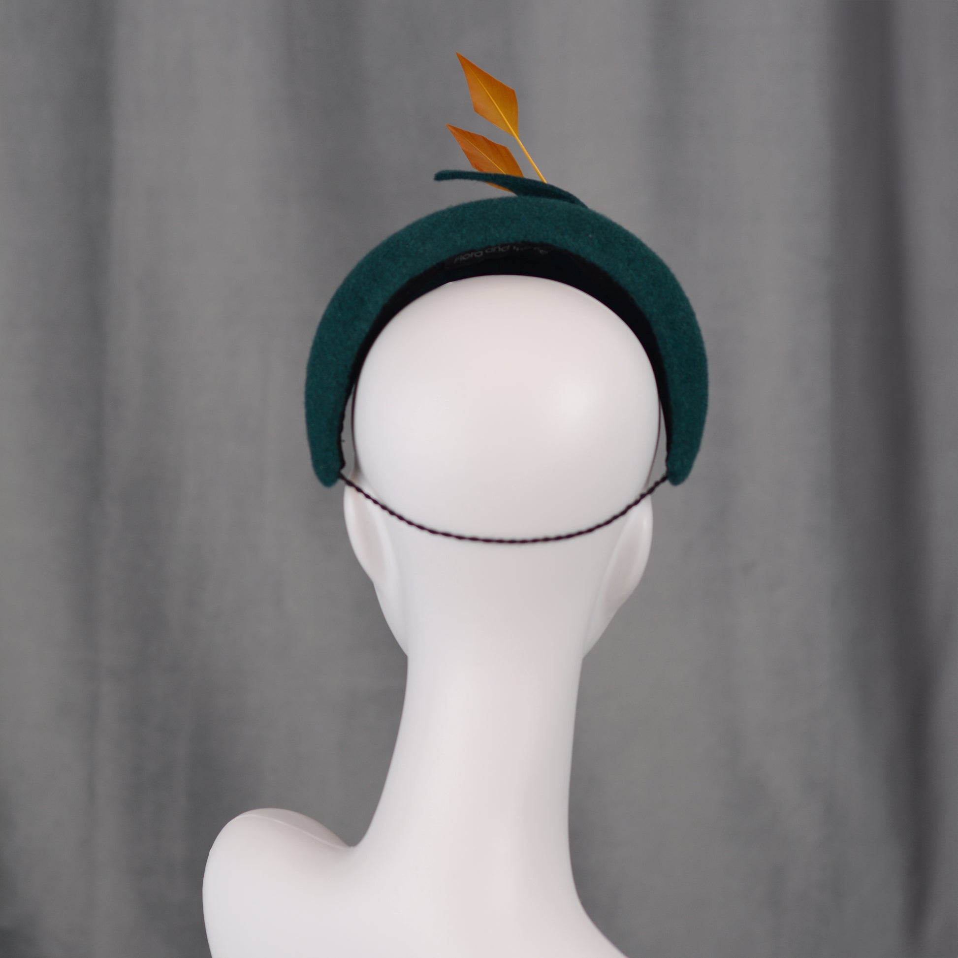 Teal green headband  fascinator with gold yellow feathers and bow on a gray background