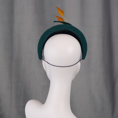 Teal green headband  fascinator with gold yellow feathers and bow on a gray background