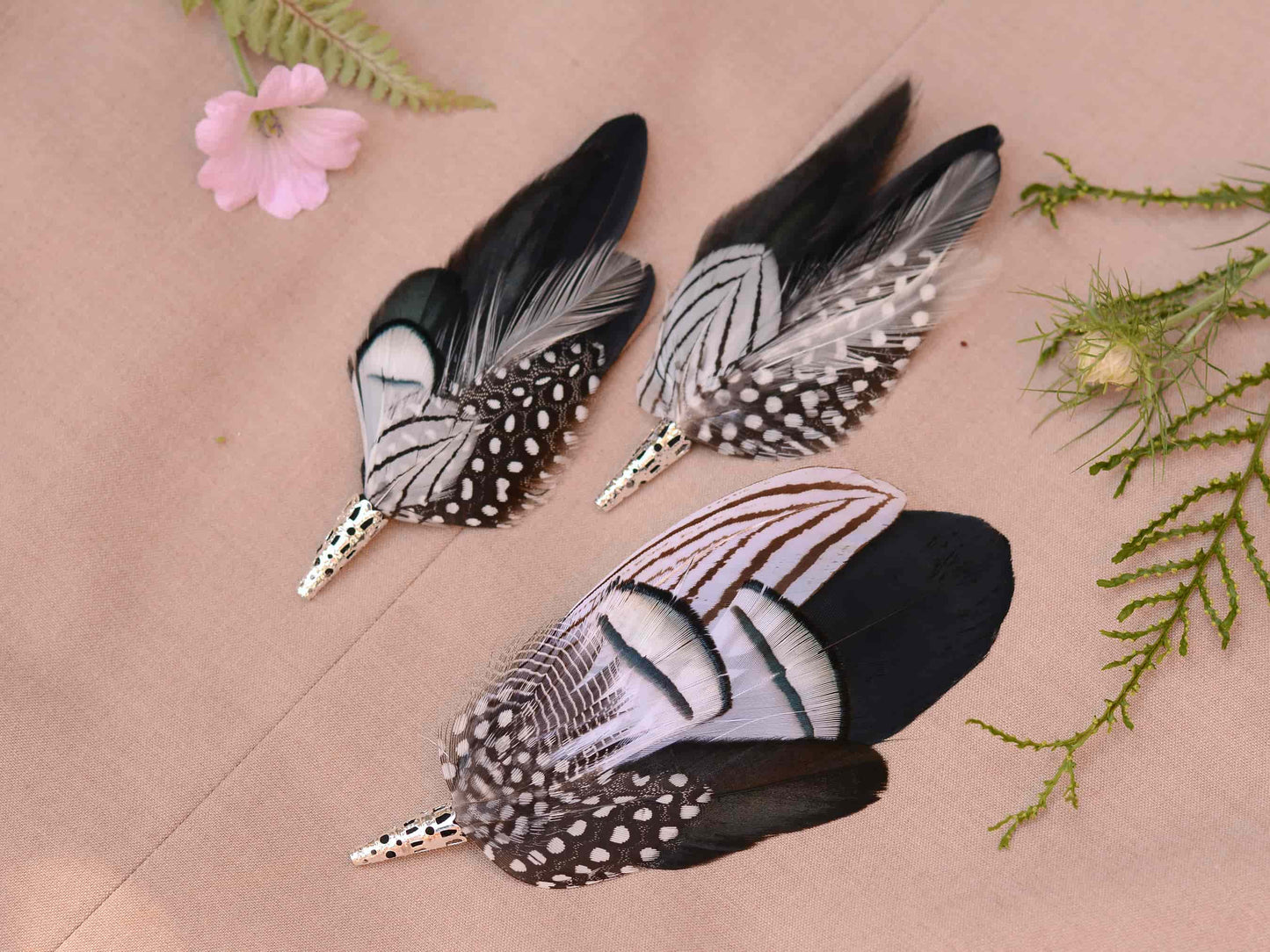 Set of 3 matching feather boutonniere brooches on a beige surface with floral and greenery accents
