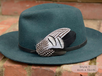 Teal fedora hat with a large decorative feather hat pin on a brick surface