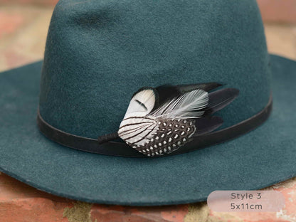 Teal hat with black and white feather hat pin feather on a textured surface