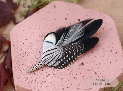 Decorative black and white feather lapel pin with  metal cap on a pink textured surface