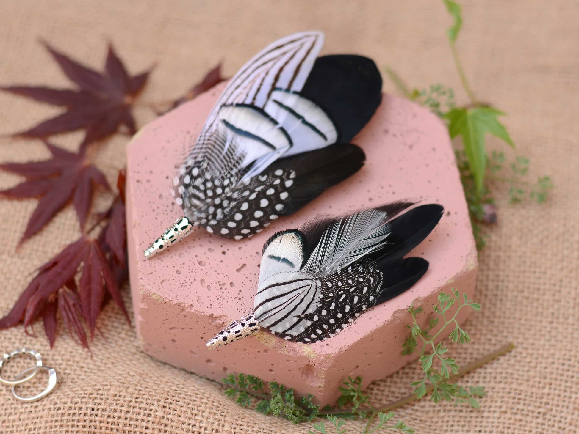 Feathered brooches on a pink stone with leaves and greenery in the background