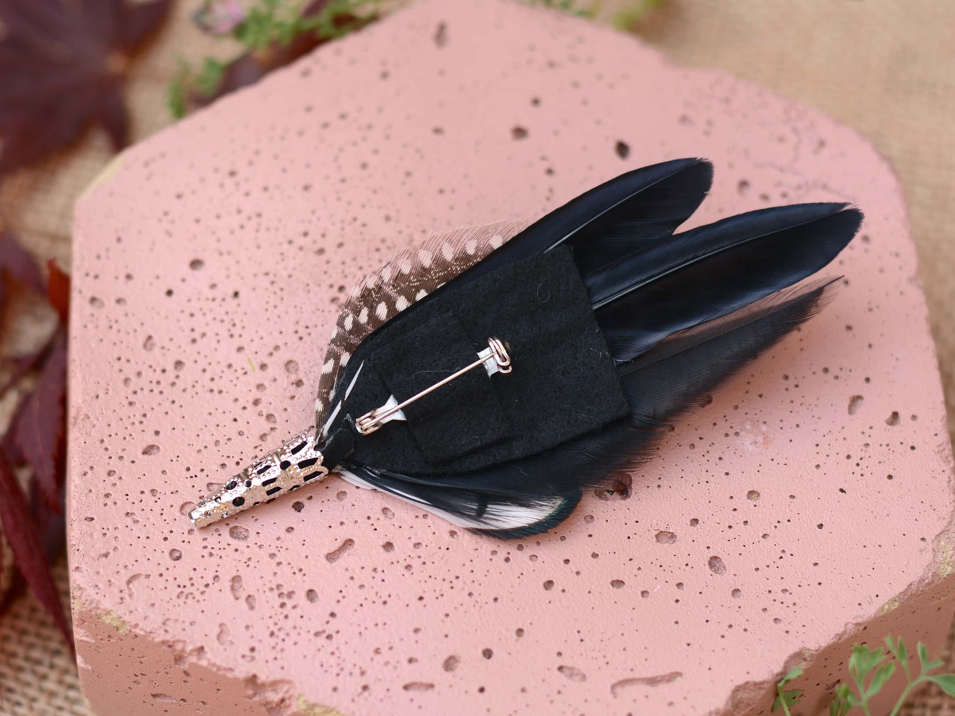 Black feathered brooch on a textured pink surface