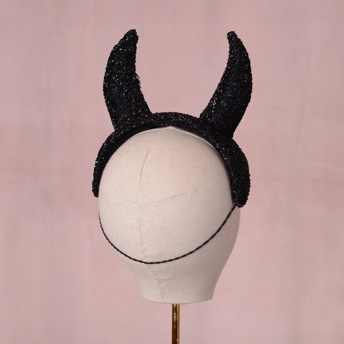 Black glittery horn headpiece displayed on a white mannequin head against a soft pink background.