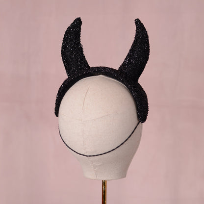 Black glittery horn headpiece displayed on a white mannequin head against a soft pink background.
