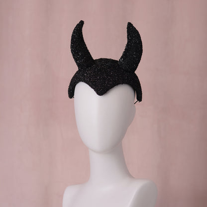 A black glittery devil horn halloween headband displayed on a white mannequin head against a soft pink background.