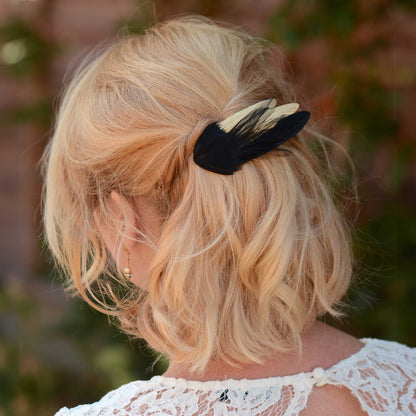 A blonde woman shown from the back wearing a black and gold feather hair accessory.