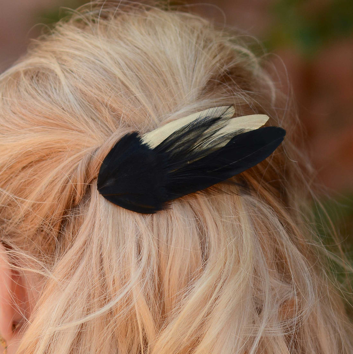 Close up of a black and gold feather hair decoration clipped into a loose wavy blonde hair style.