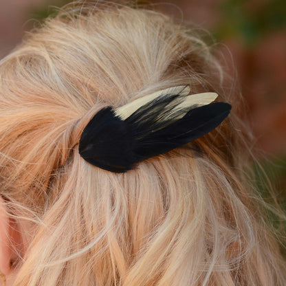 Close up of a black and gold feather hair decoration clipped into a loose wavy blonde hair style.