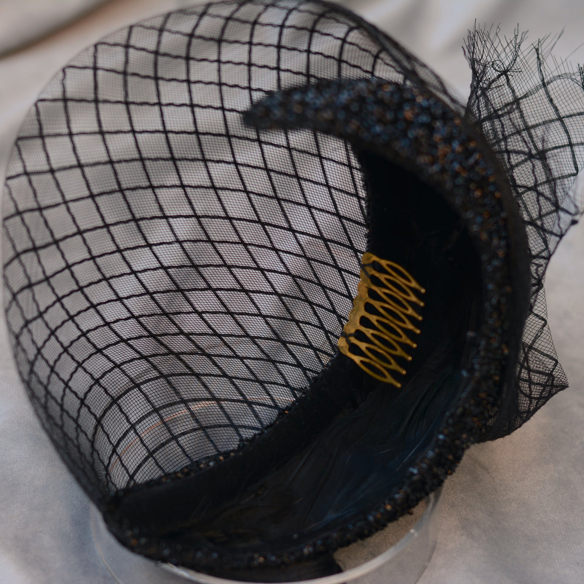 Black veiled headband headpiece with a gold-toned comb on a grey background
