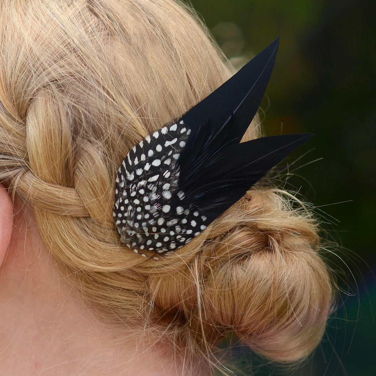 A close-up of a blonde woman's braided hair bun decorated with a black and white spotted feather hair accessory.