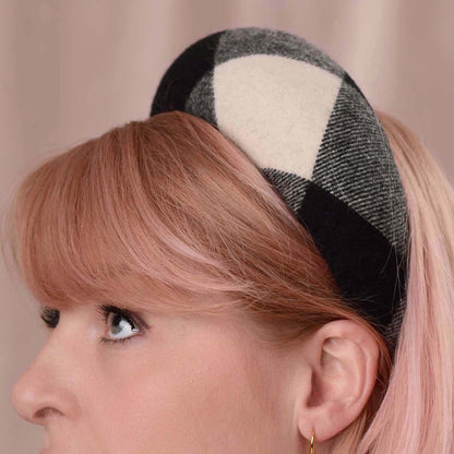 A close-up of a woman with pink hair wearing a black and cream plaid raised headband fascinator.