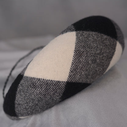 A black, white, and grey checked wool headband fascinator. The hat is displayed on a white mannequin head. The checked pattern is made up of large squares.