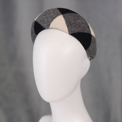 A black, white, and grey checked wool headband fascinator. The hat is displayed on a white mannequin head. The checked pattern is made up of large squares.