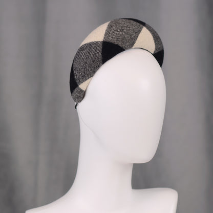 A black, white, and grey checked wool headband fascinator. The hat is displayed on a white mannequin head. The checked pattern is made up of large squares.