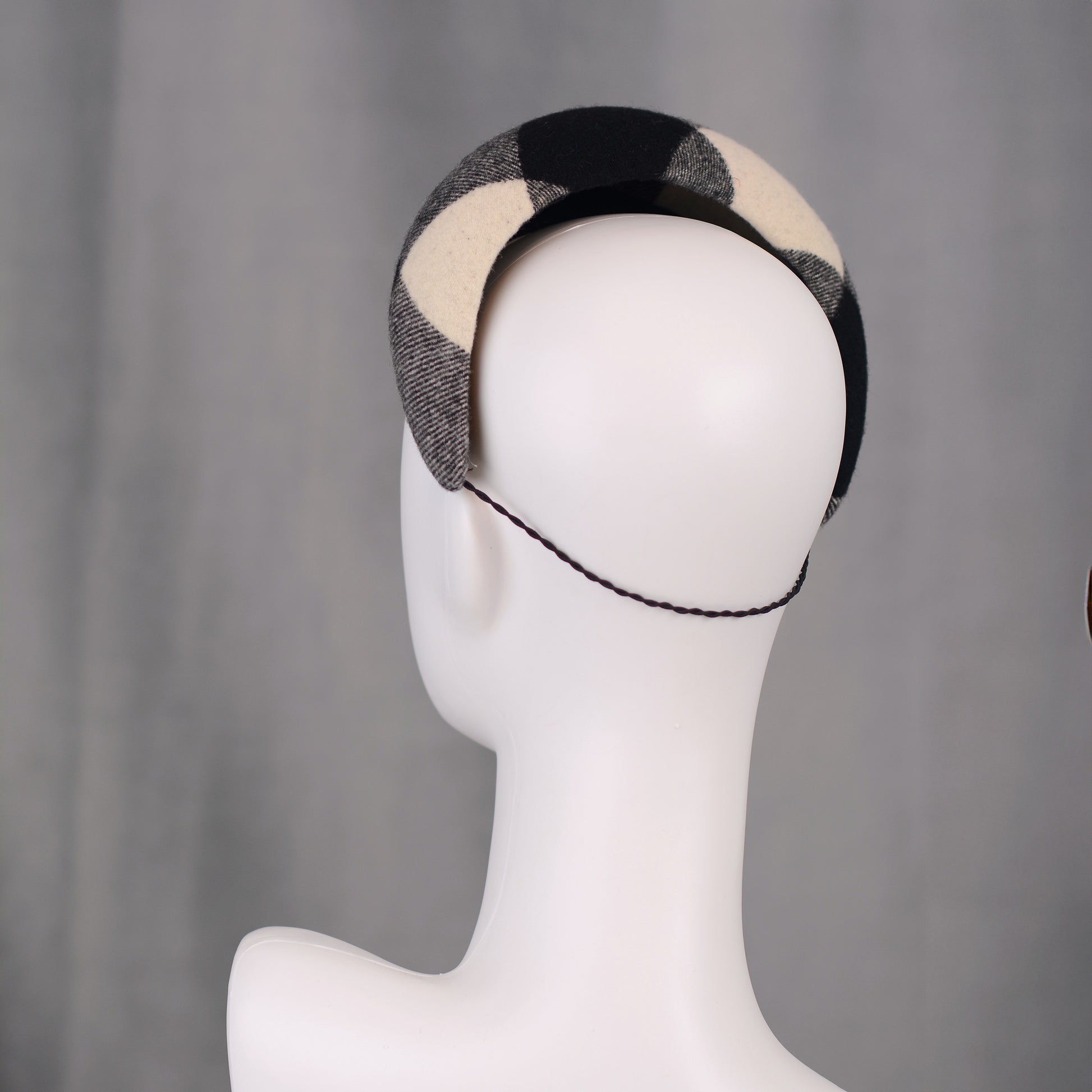 A black, white, and grey checked wool headband fascinator. The hat is displayed on a white mannequin head. The checked pattern is made up of large squares.