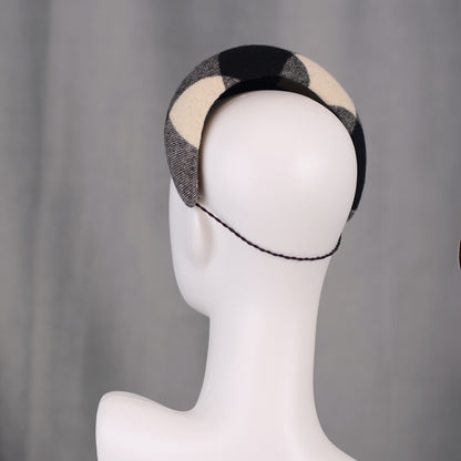 A black, white, and grey checked wool headband fascinator. The hat is displayed on a white mannequin head. The checked pattern is made up of large squares.