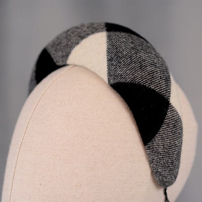 A black, white, and grey checked wool headband fascinator. The hat is displayed on a white mannequin head. The checked pattern is made up of large squares.