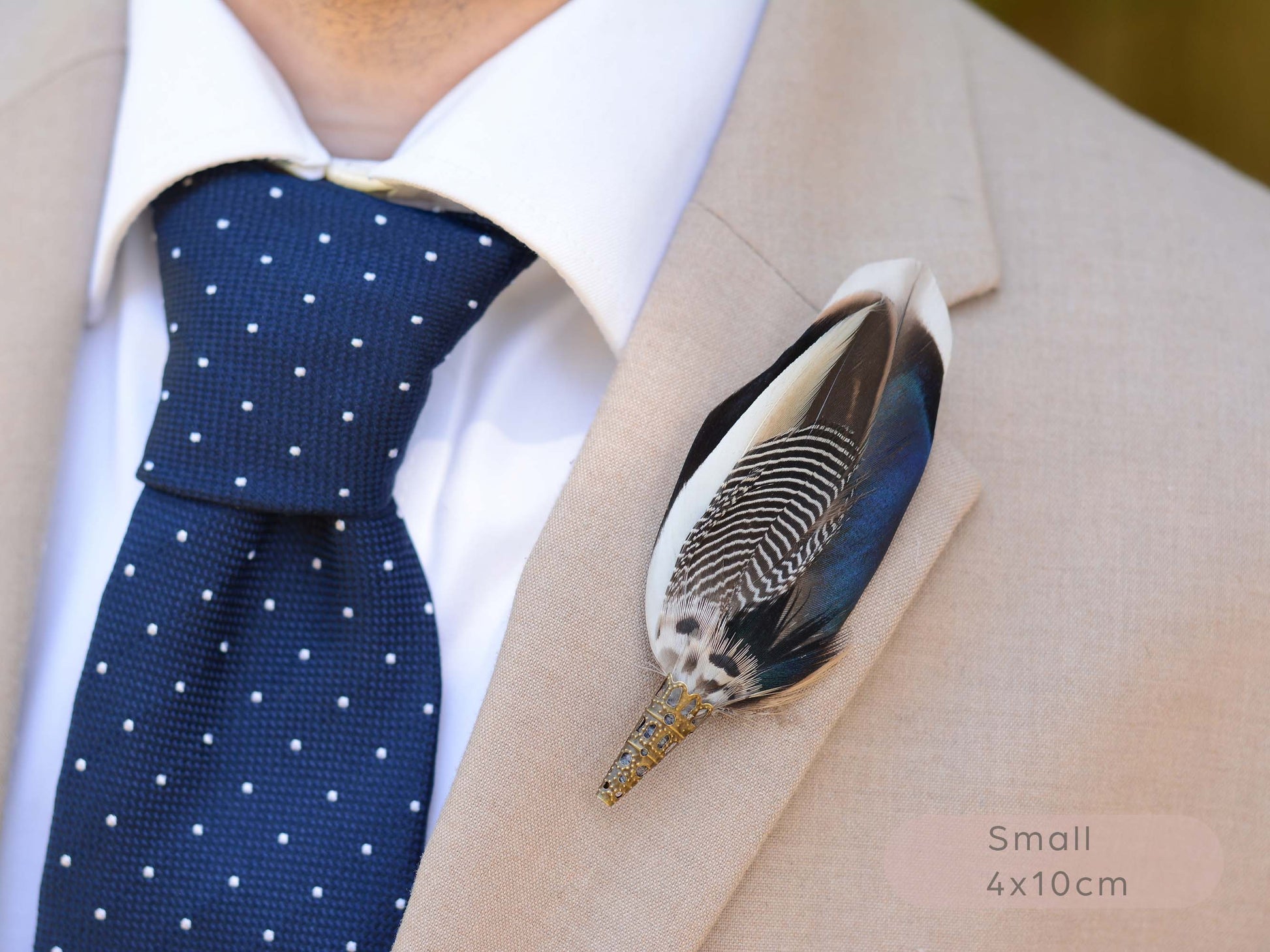 A close-up front view of a beige suit jacket worn with a white dress shirt, navy polka-dot tie, and a decorative duck feather lapel pin. The pin has black-and-white striped detailing with blue, black, and white feathers.