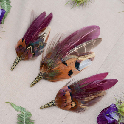 Three feathered wedding boutonnieres on a beige fabric background surounde by flowers and plants