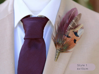 Maroon and pheasant feather lapel pin accessory on a beige suit jacket with a maroon tie.